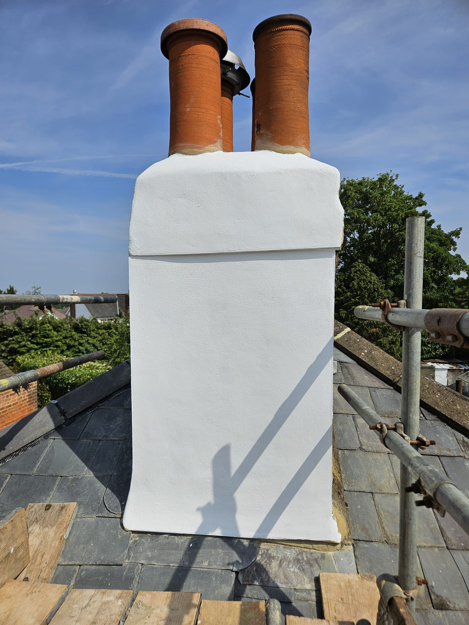 Rebuilt and rendered chimney stack with new flaunching on a slate roof in Surrey