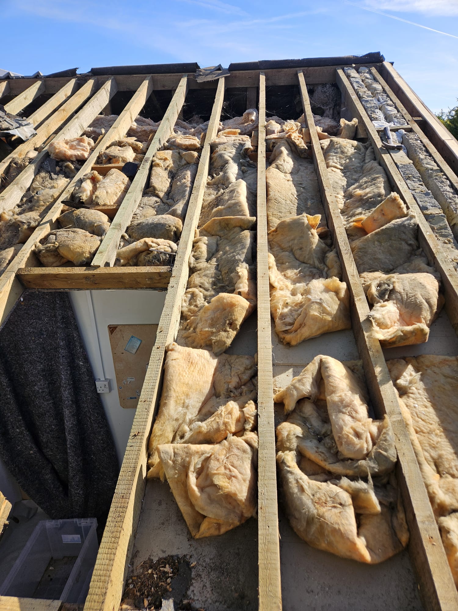 Roof stripped to the rafters with old insulation exposed before a new roof in Surrey