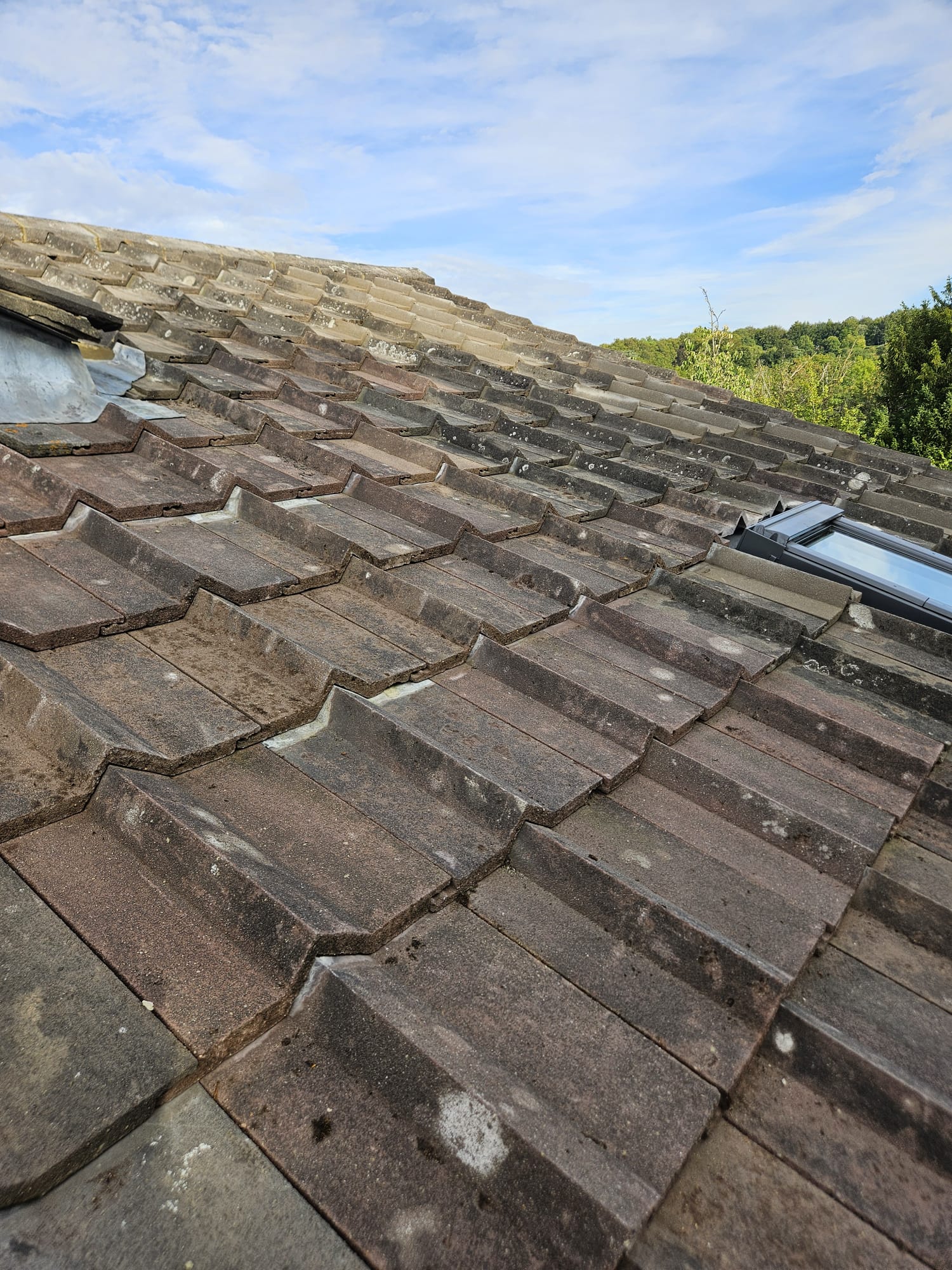 Weathered concrete roof tiles on a Surrey roof beside a roof window